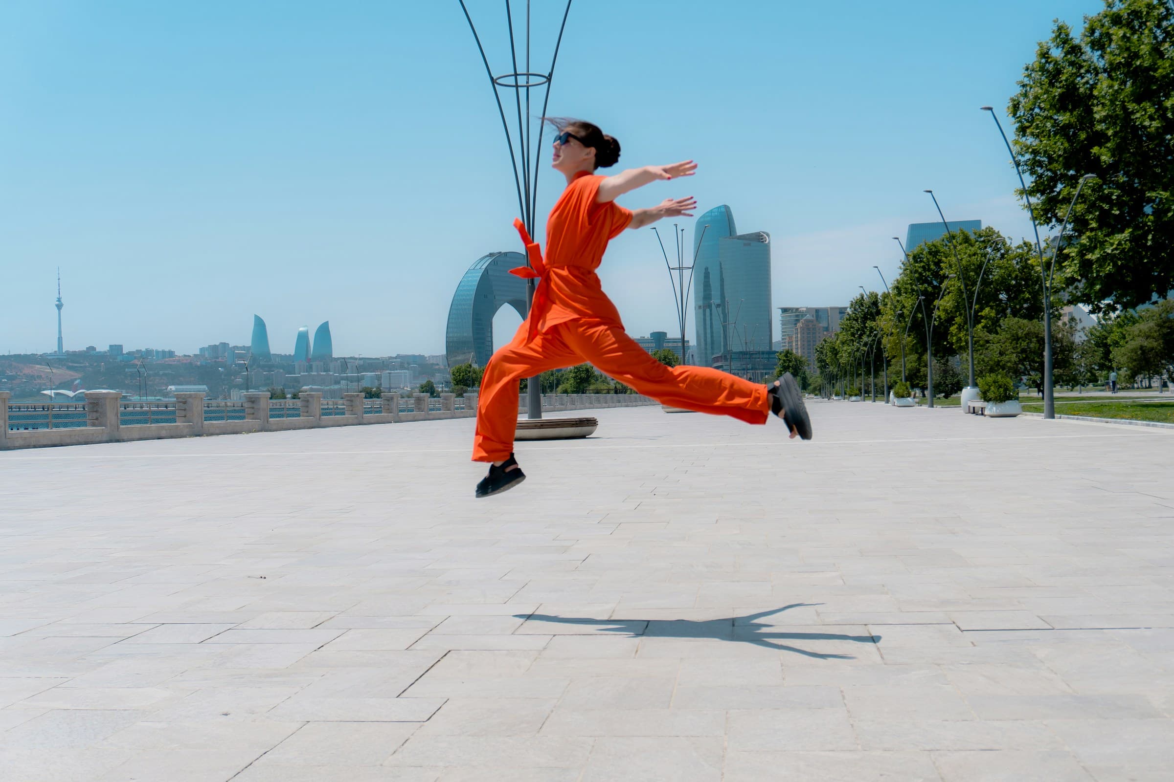 A woman in an orange jumpsuit mid-leap against a blue sky