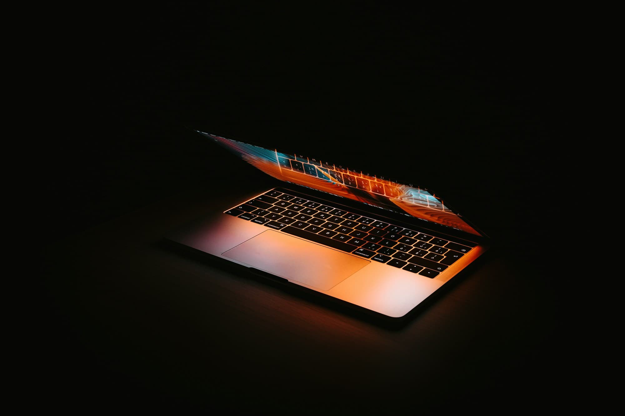 Laptop half open on black, its screen glowing orange